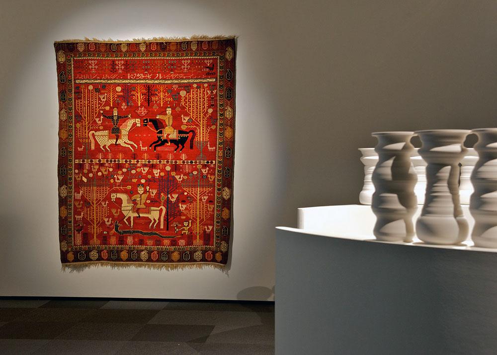 A contemporary Afghan rug alongside a work by Greg Payce at “We Tell Ourselves Stories” at the Nickle Galleries
