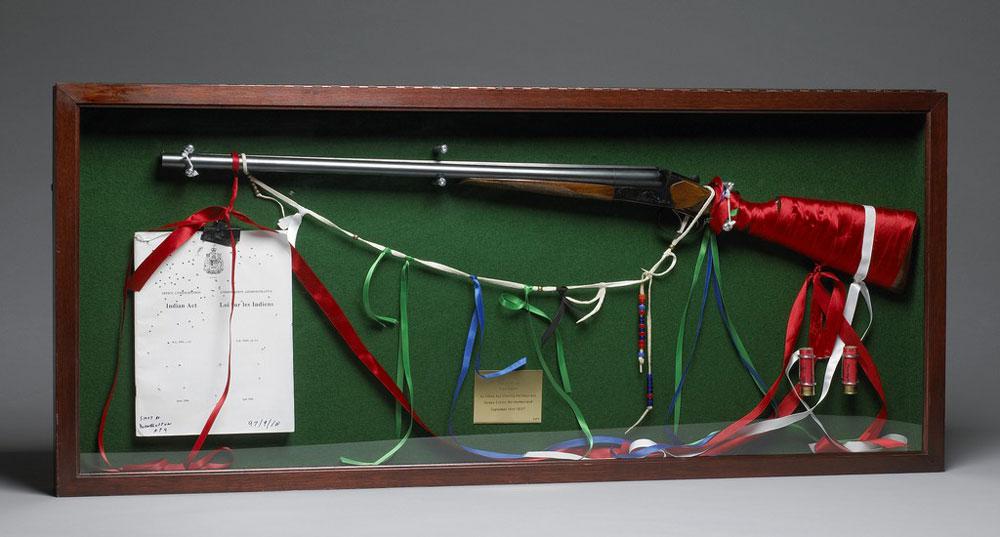Lawrence Paul Yuxweluptun <em>An Indian Act Shooting the Indian Act, Healey Estate Northumberland September 14th, 1997</em> 1997 Rifle, ribbon, used bullet shells and paper in display frame 55 cm x 1.26 m overall Courtesy National Gallery of Canada / photo &copy; NGC
