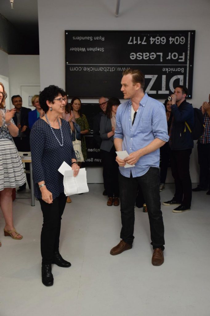 Joseph Staples (in blue shirt, foreground) receives the Contemporary Art Society of Vancouver's Emerging Artist's Prize from the CASV's Rachel Rosenfield Lafo on May 22, 2014. Some of his new real-estate-based works hang in the background.