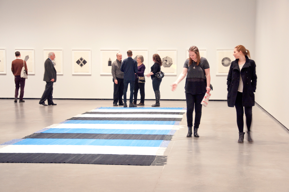 Visitors consider Brent Wadden's woven rug work <em>Keystone XL #2</em> and prints by Michael Morris at the opening of "The Blur in Between" at the Art Gallery of Alberta.  Photo: Alex Keays