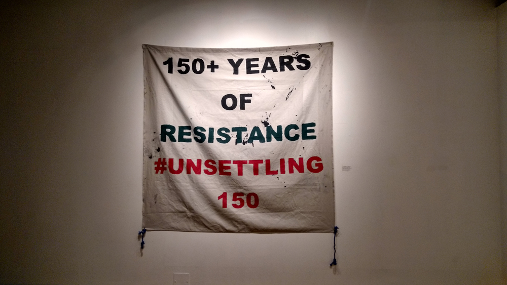 The banner that anonymous activists obstructed Themuseum's Canadian flag with now hangs in its exhibition, “A Cause for Celebration? First Things First.” Photo courtesy Themuseum.