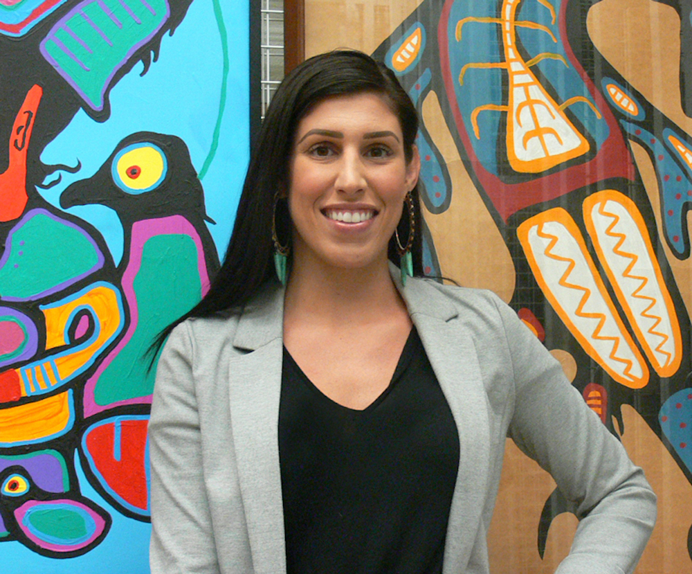 Rhéanne Chartrand, the McMaster Museum of Art's new full time curator of Indigenous art, with Norval Morriseau's <em>Transformation</em> (1995) and <em>Untitled (Thunderbird)</em> (c.1960-1964) behind her. 
