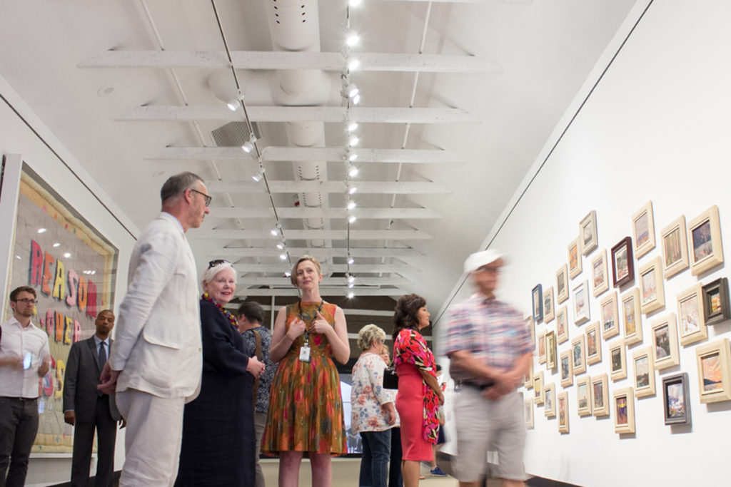 McMichael chief curator Sarah Stanners (centre, in orange) discusses “Passion Over Reason: Tom Thomson &amp; Joyce Wieland” with Lieutenant Governor Elizabeth Dowdeswell and McMichael CEO Ian Dejardin. Photo: Courtesy McMichael Canadian Art Collection.