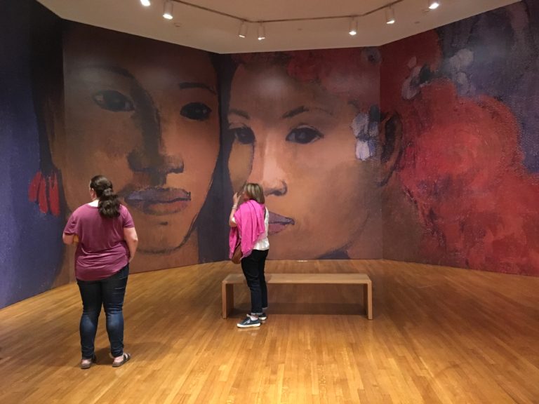 The interior to the entrance of the “Gauguin: Portraits” exhibition features two Indigenous figures from Gauguin’s painting <em>Barbarian Tales</em> (1902). The European man also pictured in the painting is cropped out. Photo: Leah Sandals.