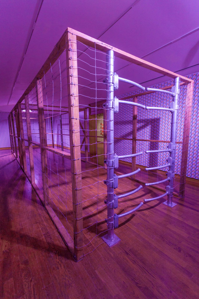 A view of Ursula Johnson’s <em>Moose Fence</em>, a large sculptural installation with lighting and a galvanized gate and cage.