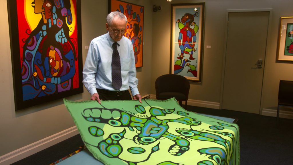 Art dealer Donald Robinson of Kinsman Robinson galleries examines the painting at the centre of a Norval Morrisseau forgeries case in a scene from the new documentary <em>There Are No Fakes</em>.