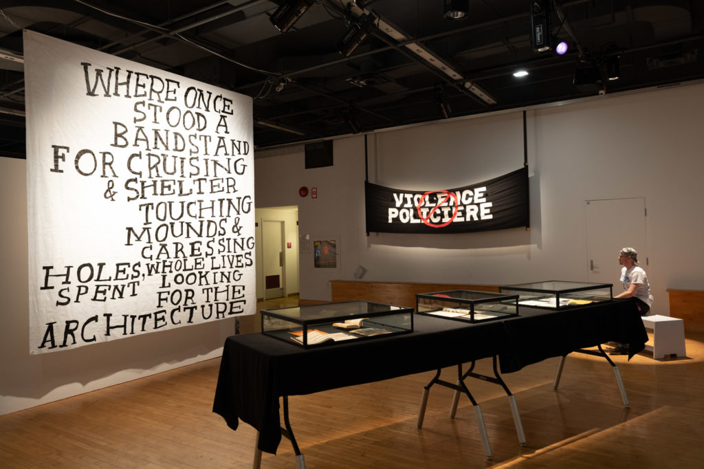 Hazel Meyer, <em>Where Once Stood A Bandstand for Cruising & Shelter</em>, 2017. Paint on Tyvek; Anonymous creator, <em>Police Brutality</em>, 1990. Banner courtesy les Archives Gaies du Québec. Installation view of 