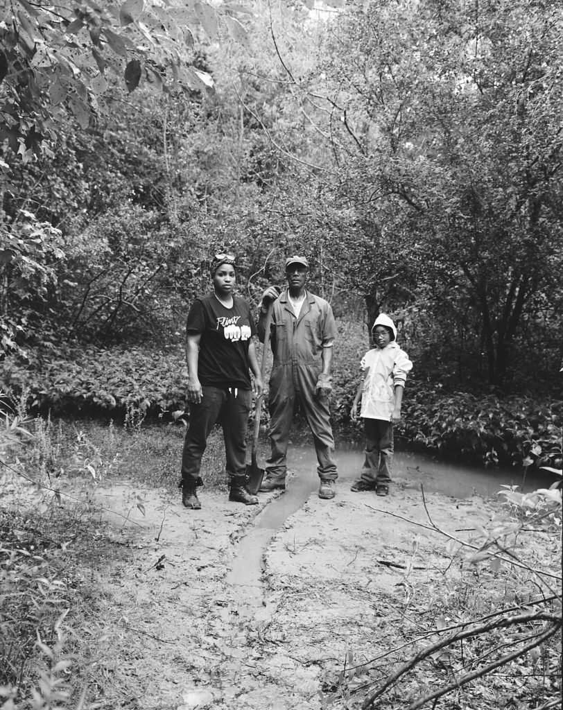LaToya Ruby Frazier, <em>Mr. Smiley standing with his daughter Shea and his granddaughter Zion on their fresh water spring, Jasper County, Newton, Mississippi</em>, from the series <em>Flint is Family II</em>, 2017. Black and white photograph. Courtesy Gavin Brown’s enterprise.